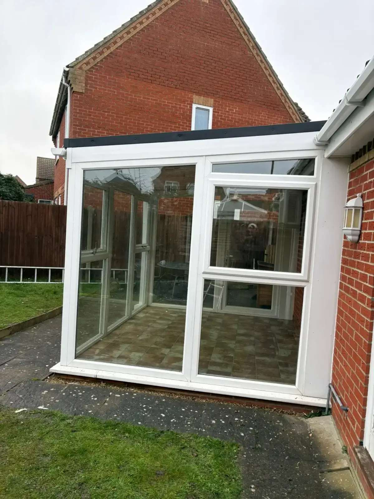 Exterior side profile of a white uPVC lean-to conservatory framework on a red brick home extension. Installed by Norfolk Exterior Solutions